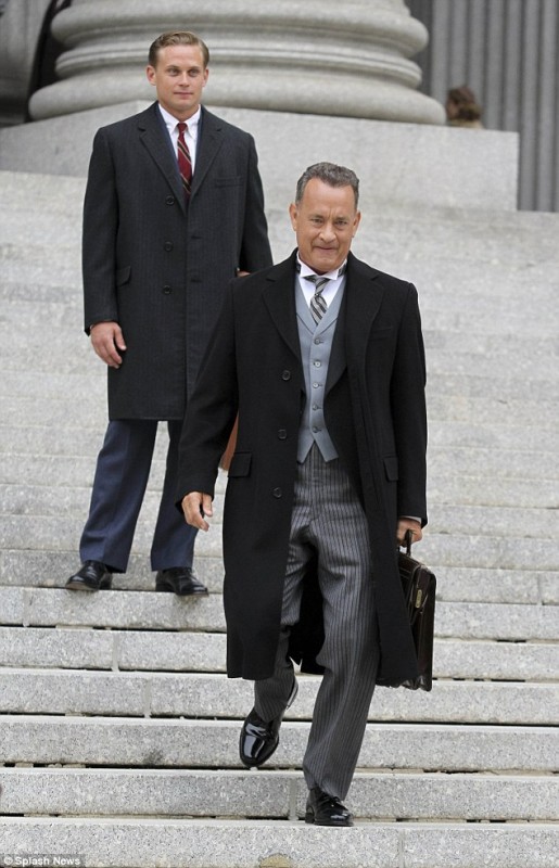 Tom Hanks in a traditional classic three-piece suit and a large black overcoat is joined on set by co-star Billy Magnussen